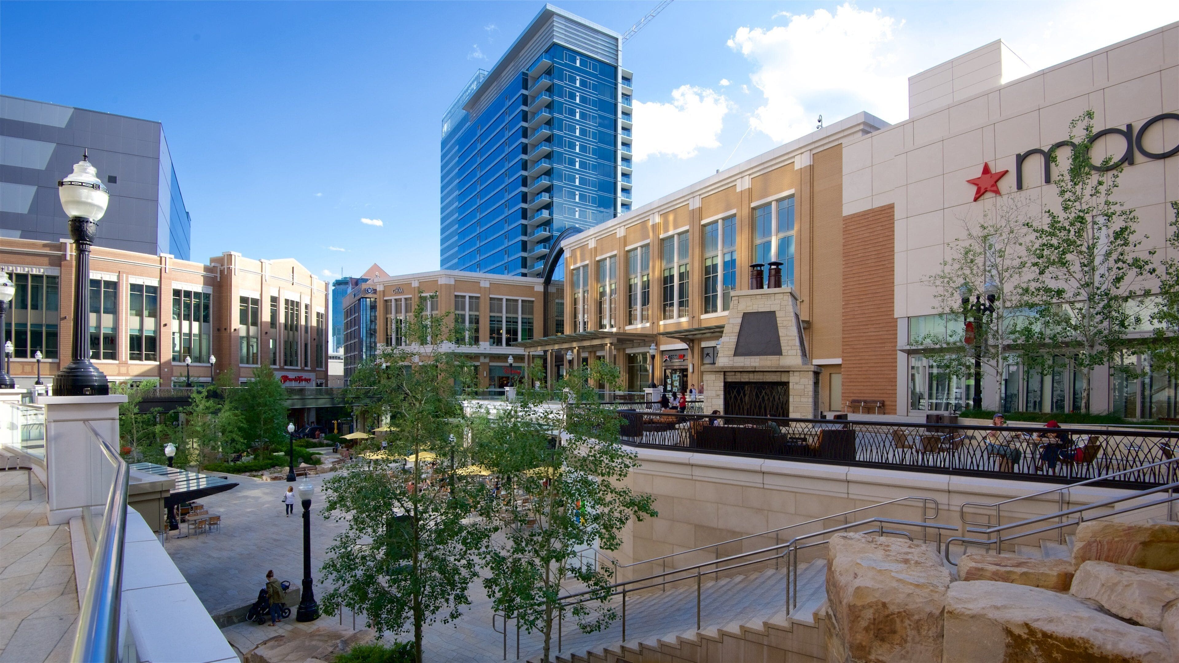 A shopping plaza with a Macy's store, outdoor seating, and a modern building in the background.