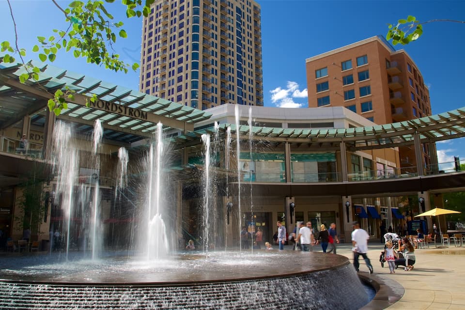 A public fountain with multiple water jets, surrounded by a covered walkway and modern buildings.