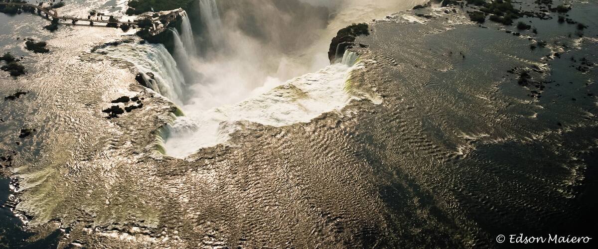 A large waterfall with mist rising from the base, surrounded by water and greenery.