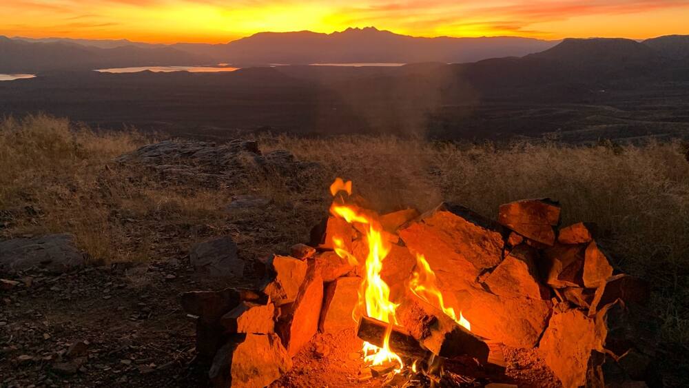 A campfire at sunset with mountains in the background.
