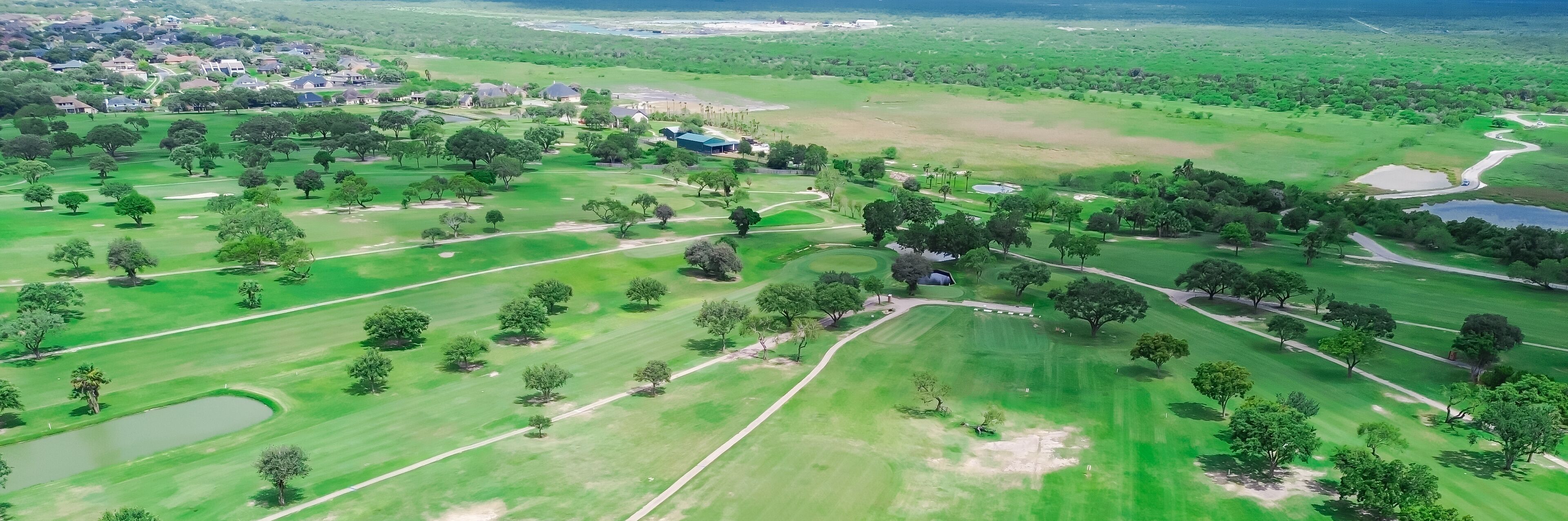 Panorama aerial view country golf course with sand trap, club cars pathway, grassy fairway, lush green tall mature trees near Hazel Bazemore Park and Nueces River in Corpus Christi, South Texas