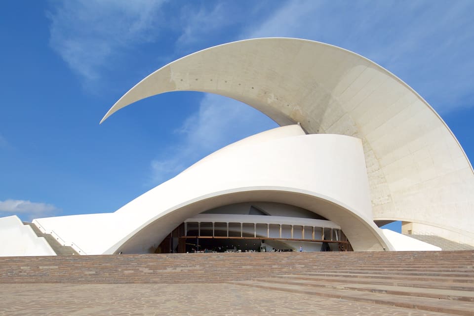 A modern architectural building with a large white curved roof and a stone staircase leading up to it.