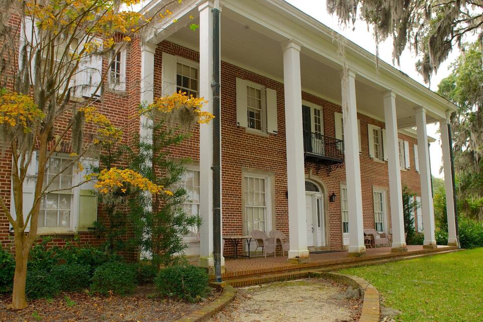 A large brick building with a white porch and columns, surrounded by trees and a well-maintained lawn.