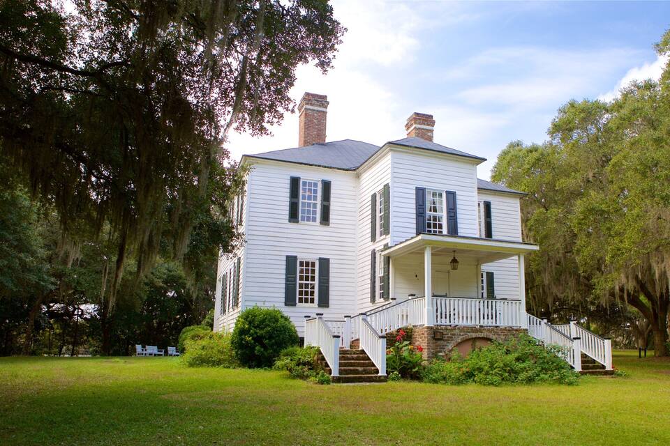 A large white house with green shutters, a porch, and a brick archway.