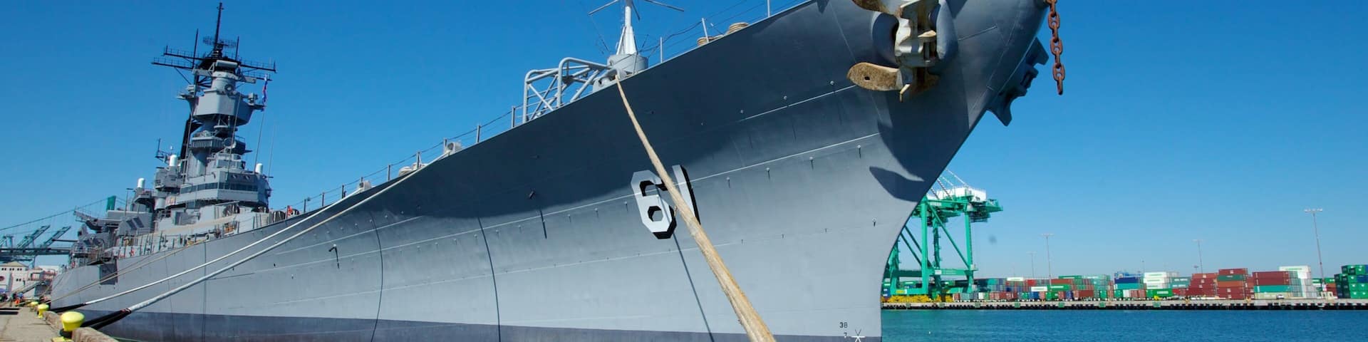 Un gran buque de guerra atracado en un puerto bajo un cielo azul despejado.