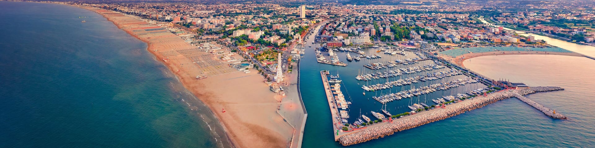 An aerial view of a coastal city with a marina, beach, and urban landscape.