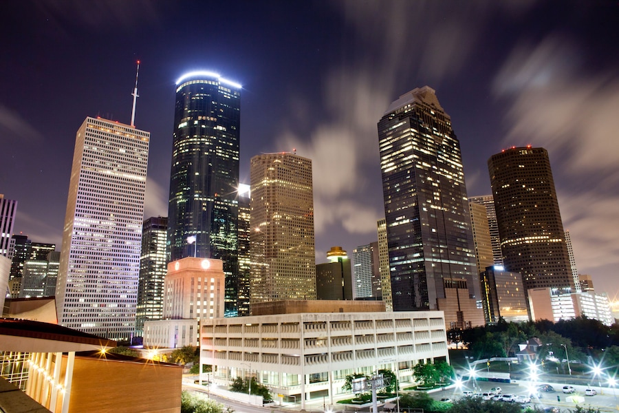 A cityscape at night with illuminated skyscrapers and a parking structure.