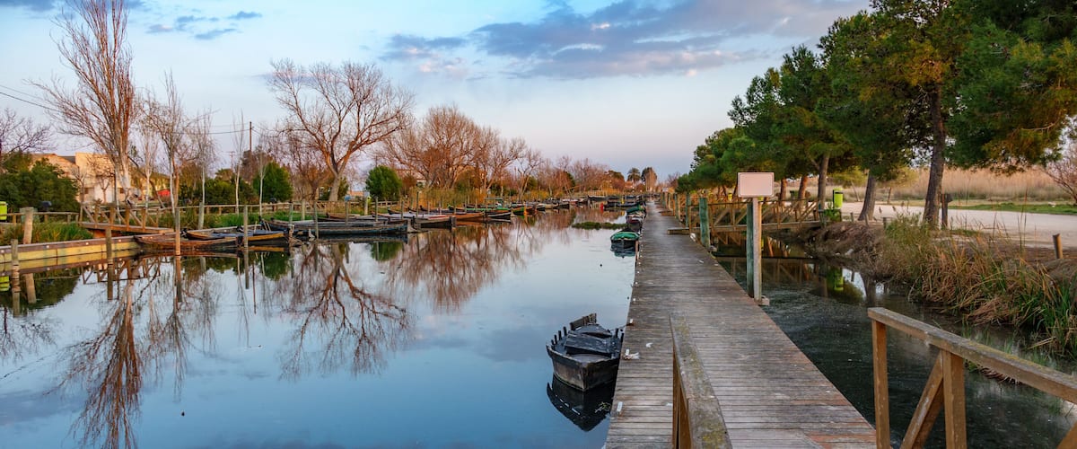 A calm river with wooden docks and boats, surrounded by trees and a clear sky.