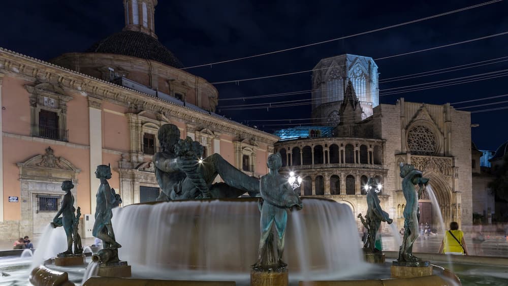Une vue nocturne d’une fontaine historique ornée de statues, entourée d’une architecture classique.