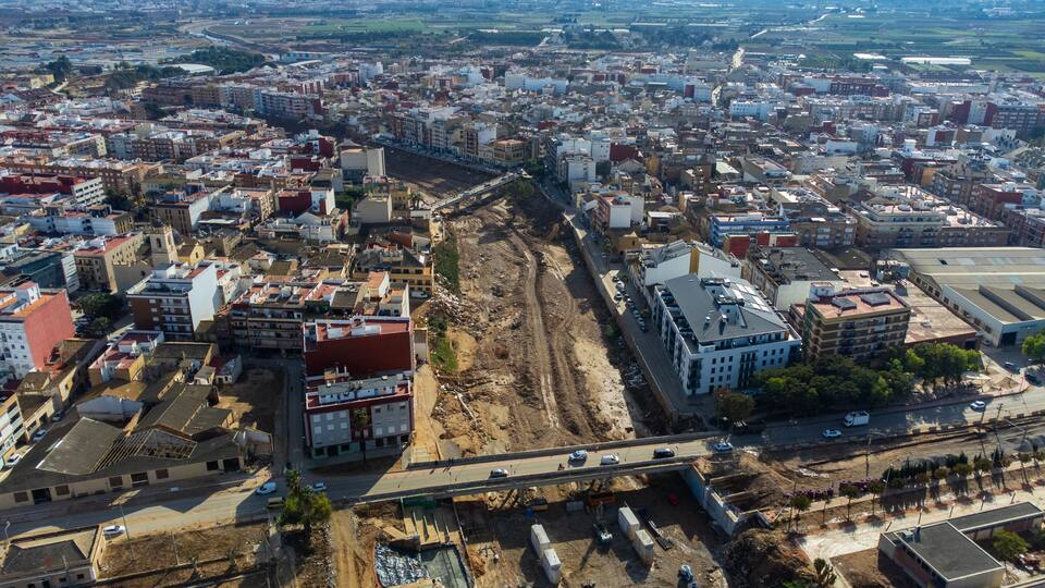 An aerial view of a city with a large construction site in the center, surrounded by dense urban buildings.