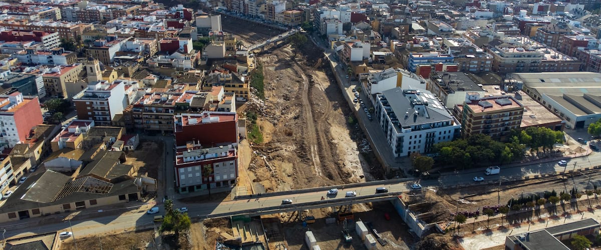 An aerial view of a city with a large construction site in the center, surrounded by dense urban buildings.