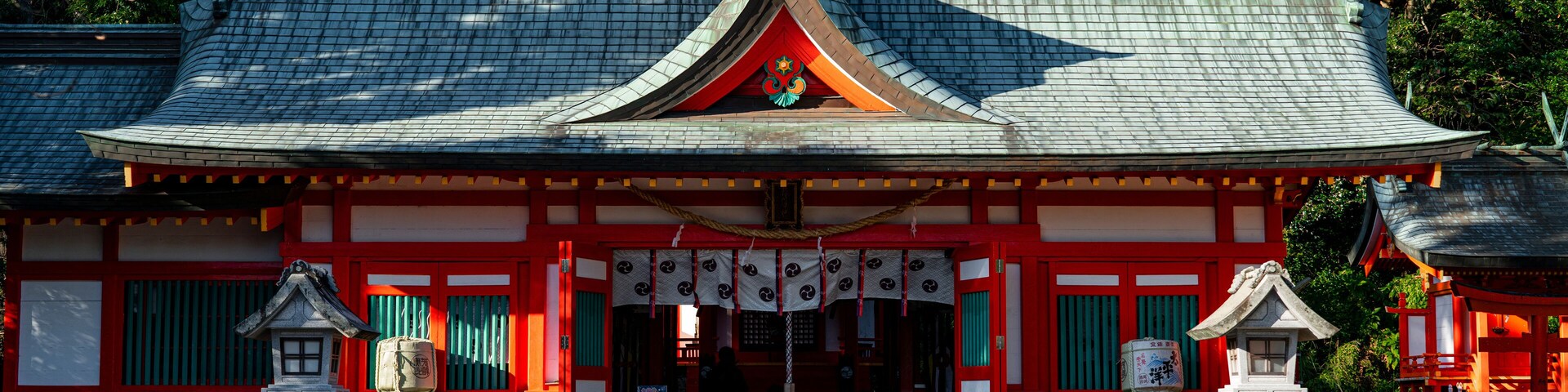 Un templo japonés tradicional con tejado de tejas, paredes rojas y blancas, y faroles de piedra.