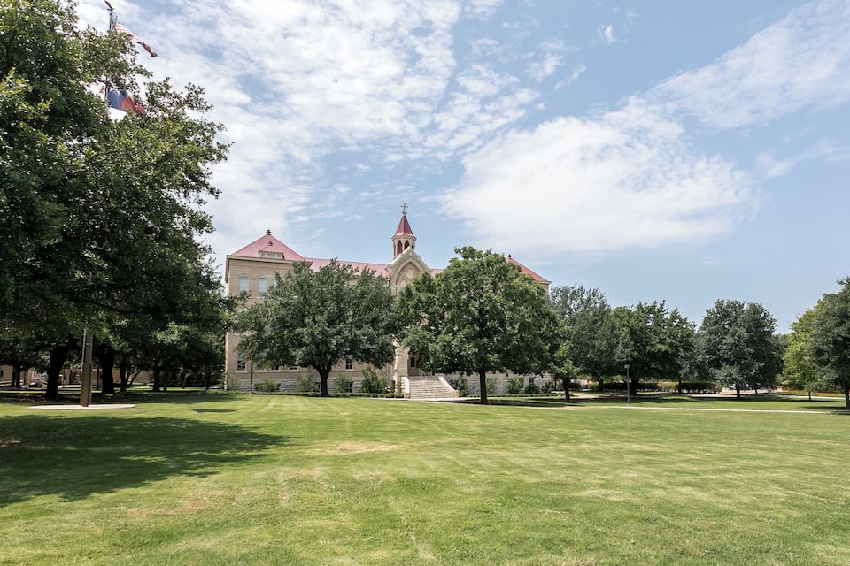 A church with a tall steeple and a red roof, surrounded by a grassy field and trees.