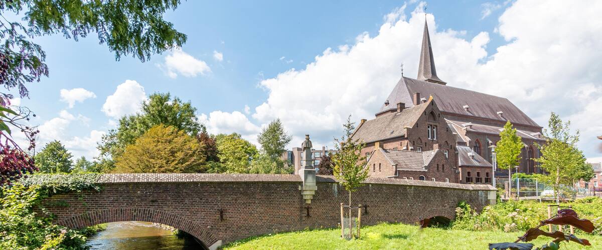 A historic church with a tall spire, a brick bridge over a canal, and lush greenery.