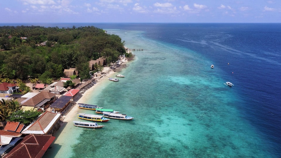 A coastal village with clear turquoise waters, a pier, and traditional houses.