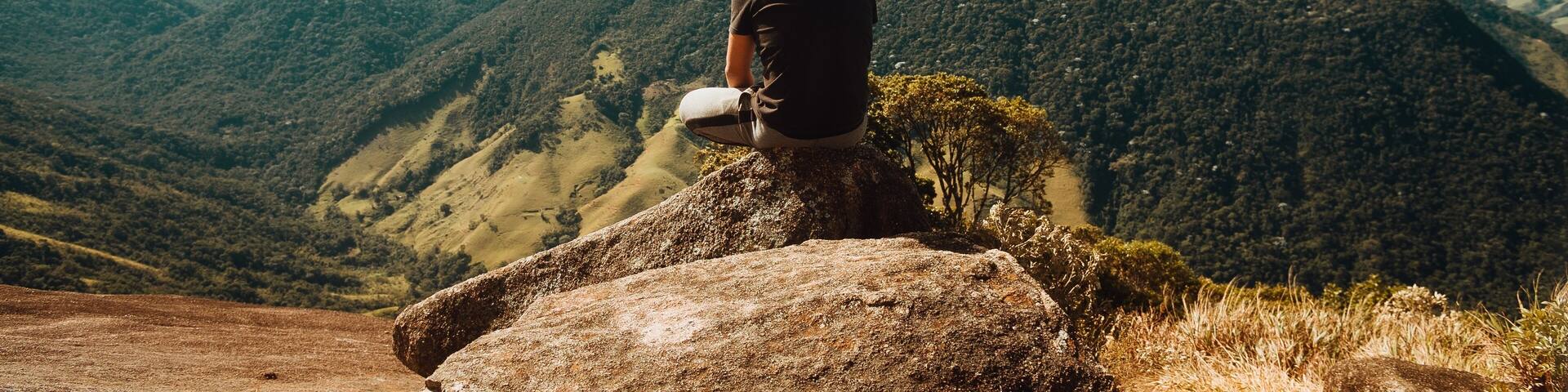 Wide shot of a person sitting on top of mountains of the Atlantic Forest in Rio De Janeiro