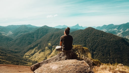 Wide shot of a person sitting on top of mountains of the Atlantic Forest in Rio De Janeiro