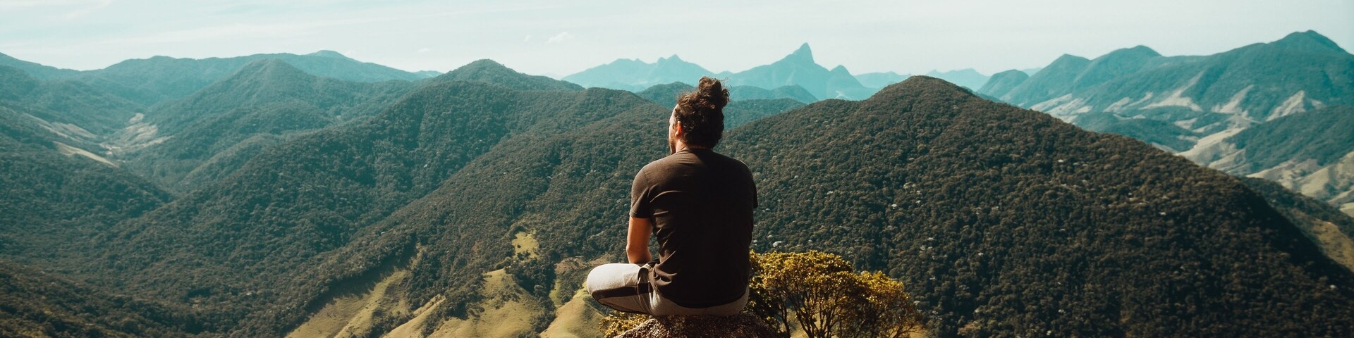 Wide shot of a person sitting on top of mountains of the Atlantic Forest in Rio De Janeiro