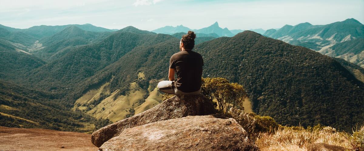 A person sitting on a rock overlooking a mountainous landscape.