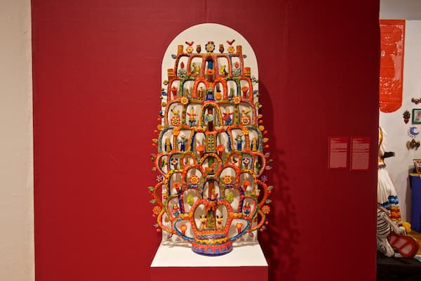 Uma instalação vibrante e detalhada de arte na parede, com um tema central de árvore, rodeada por diversas figuras e padrões.