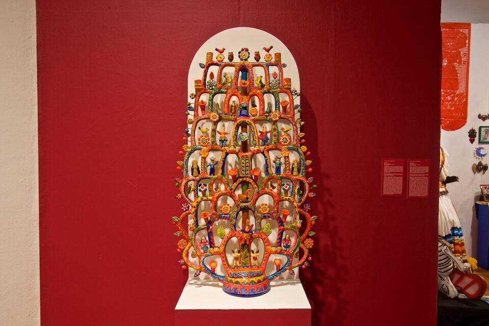 Eine farbenfrohe, detailreiche Wandgestaltung mit einem zentralen Baummotiv, umgeben von verschiedenen Figuren und Mustern.