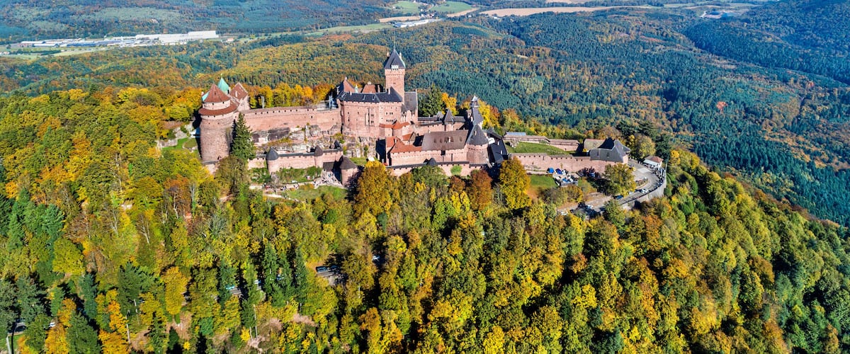 A castle surrounded by autumn-colored trees and mountains.