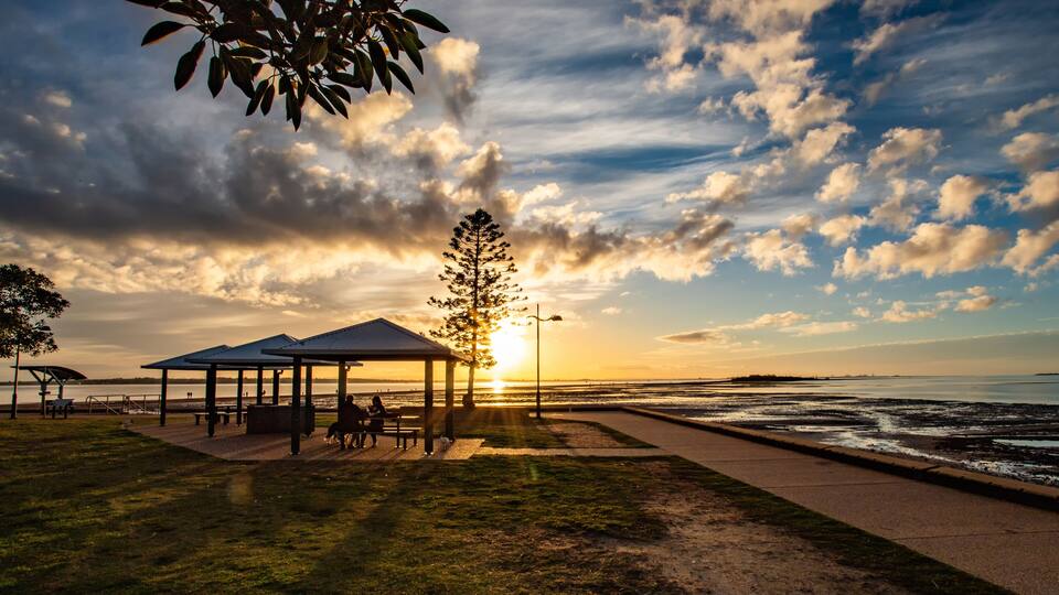 A sunset at a coastal park with a gazebo, a walking path, and a view of the ocean.
