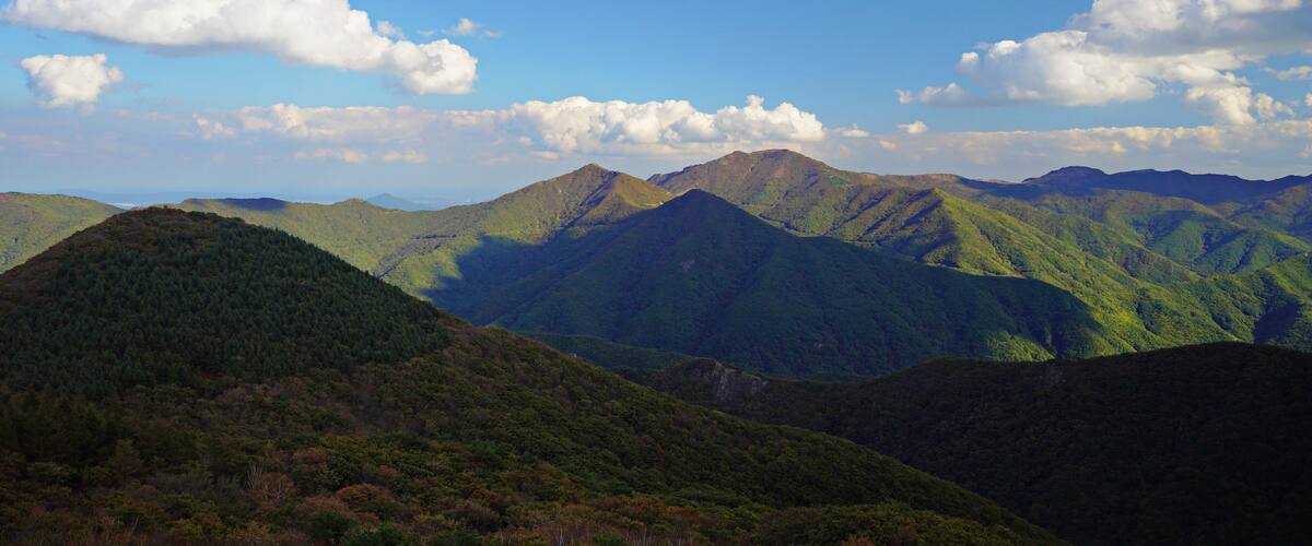 A mountainous landscape with lush green hills and a clear blue sky with scattered clouds.