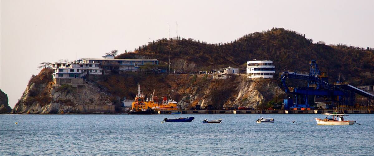 A coastal town with buildings on a cliff, boats on the water, and industrial structures.
