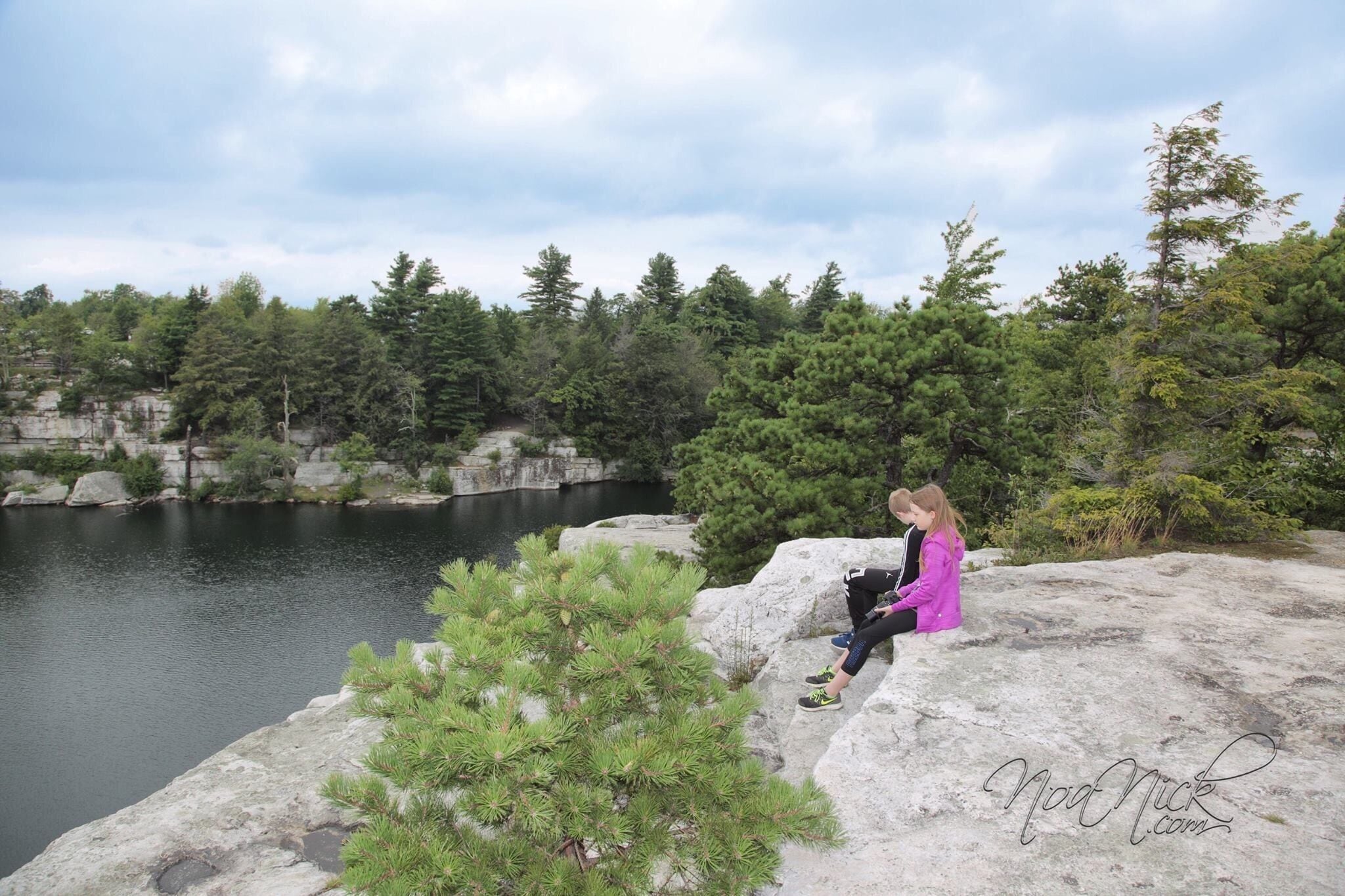 A person sitting on a rock by a lake surrounded by trees.
