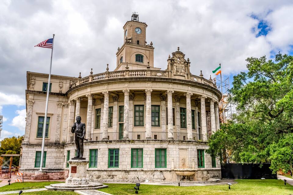 Um edifício histórico com uma rotunda central, uma estátua e duas bandeiras.