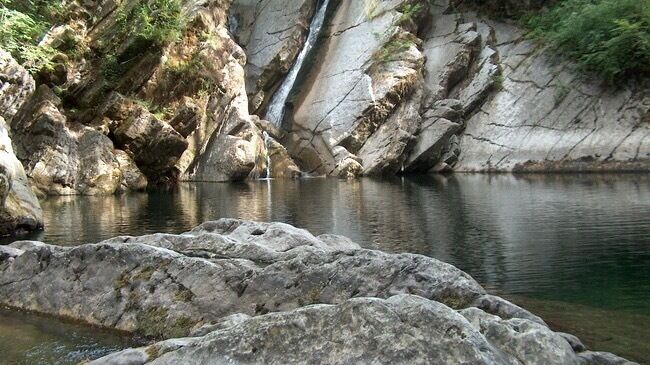 A waterfall cascading into a calm river surrounded by rocky terrain and greenery.
