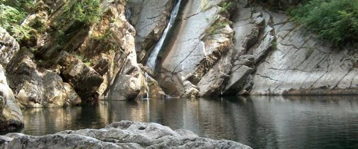 A waterfall cascading into a calm river surrounded by rocky terrain and greenery.