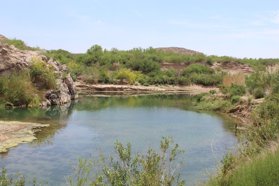 Un río tranquilo rodeado de terreno rocoso y vegetación escasa.