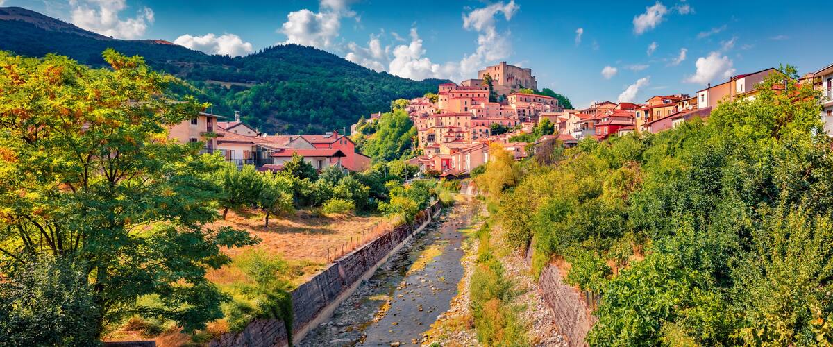 A town with red-roofed buildings, a river, and a castle on a hill.