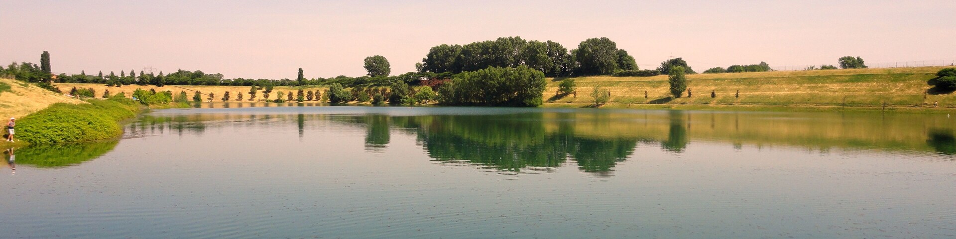 Un lago tranquilo con aguas cristalinas, rodeado de orillas cubiertas de hierba y árboles.