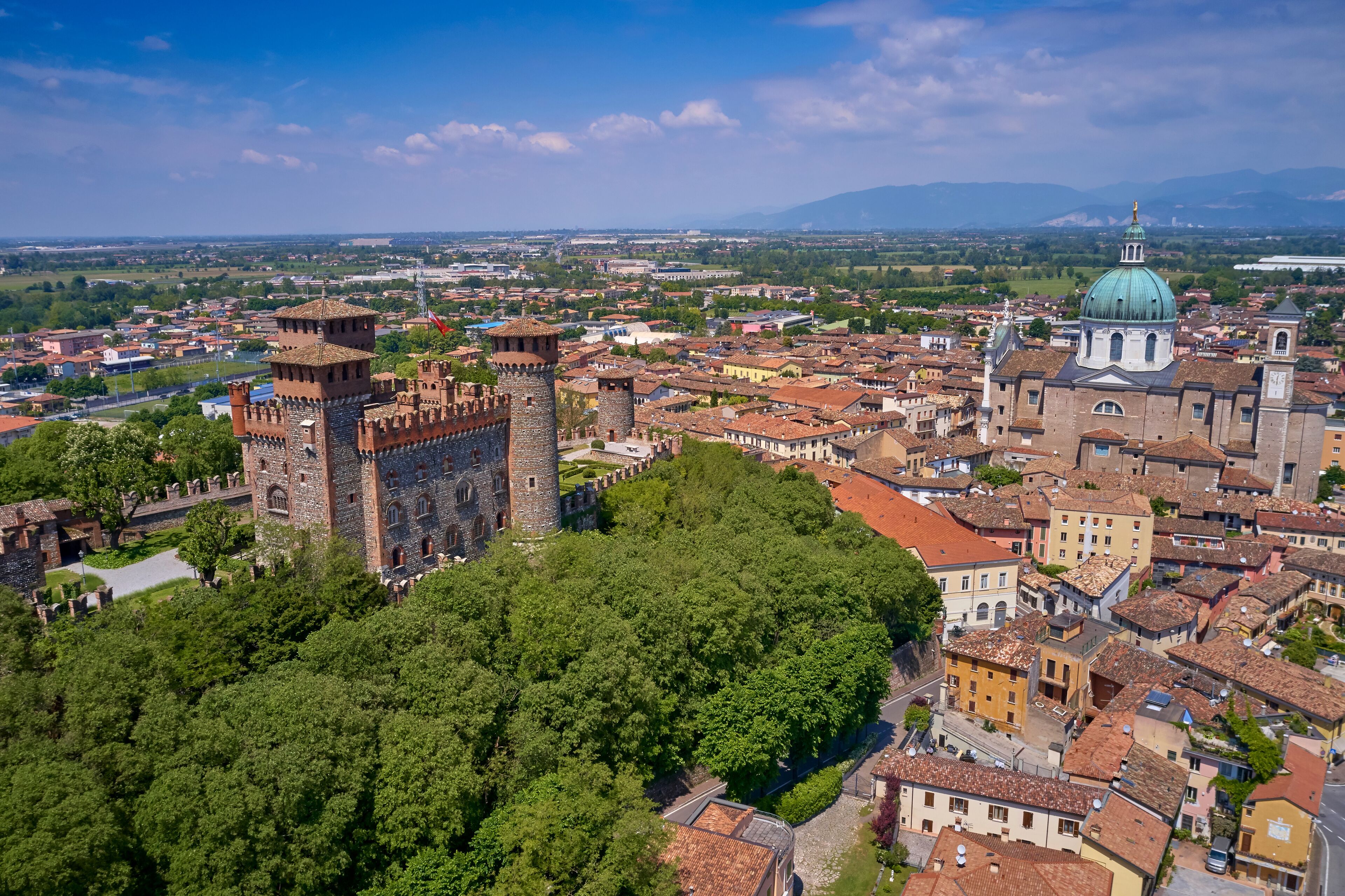 A historic city with a prominent castle, lush green trees, and a large domed church.