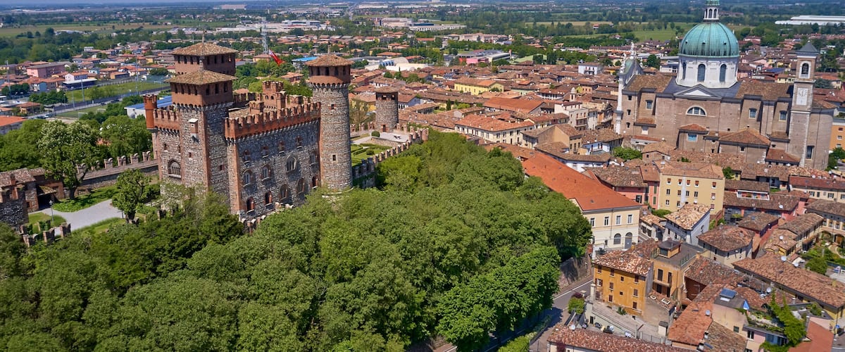 A historic city with a prominent castle, lush green trees, and a large domed church.