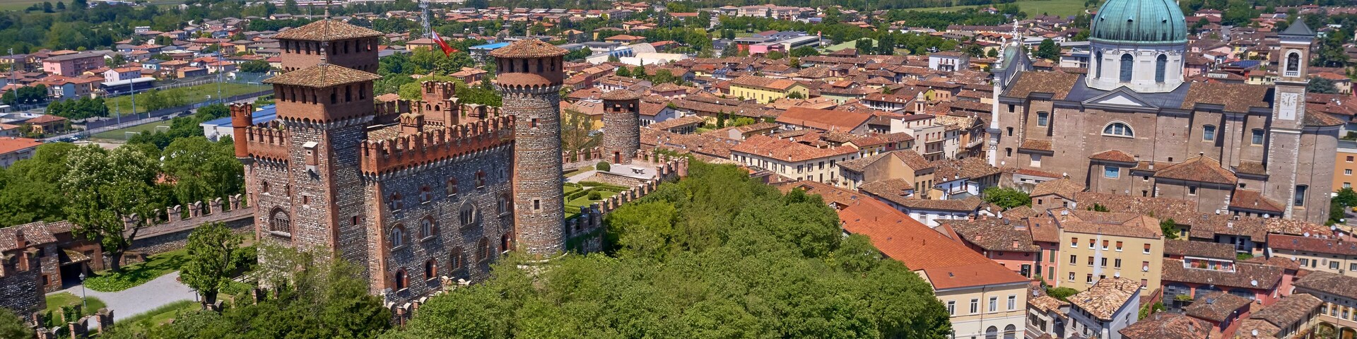 A historic city with a prominent castle, lush green trees, and a large domed church.
