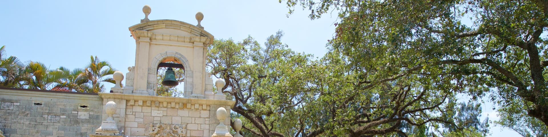 A historic building with a bell tower, arched entrance, and a courtyard with a large tree.