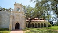 A historic building with a bell tower, arched entrance, and a courtyard with a large tree.
