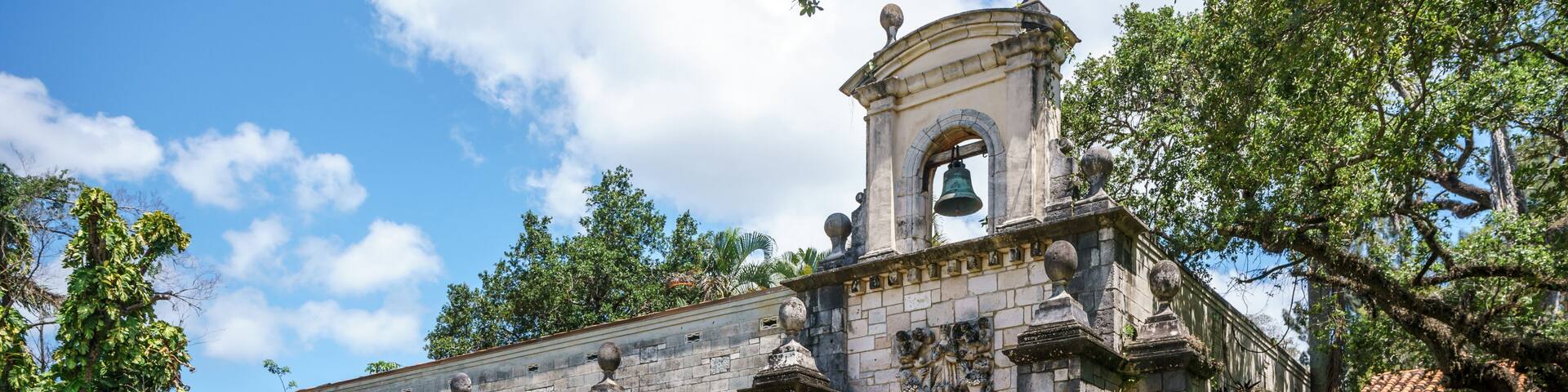 A historic stone building with a bell tower, arched windows, and a well-maintained garden.