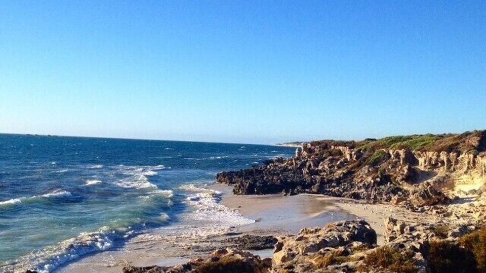 Une côte rocheuse où les vagues s’écrasent sur le rivage, sous un ciel bleu dégagé.