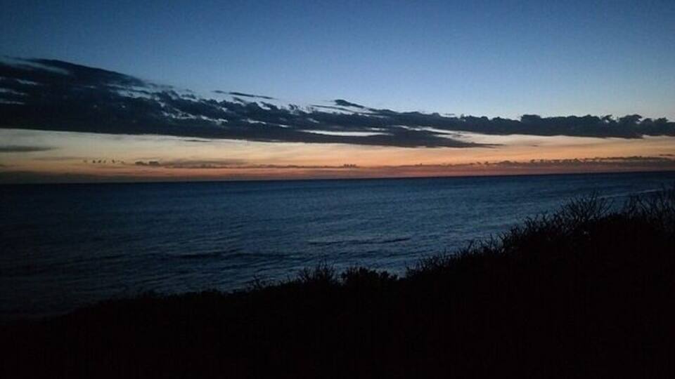 Un coucher de soleil sur la côte, avec un ciel dégagé et les silhouettes de terres lointaines.
