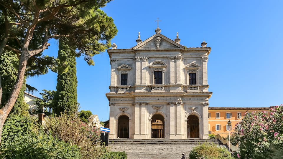 A historic church with a bell tower, surrounded by lush greenery and a clear blue sky.