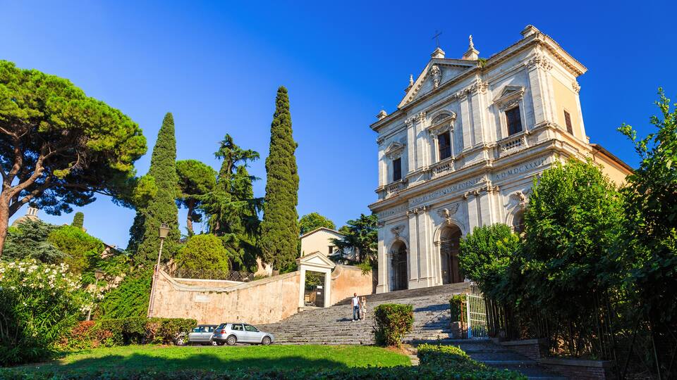 A historic building with columns and a dome, surrounded by lush greenery and trees.