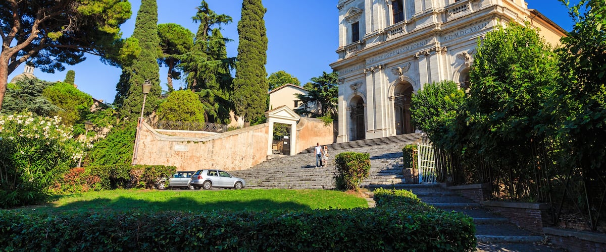 A historic building with columns and a dome, surrounded by lush greenery and trees.