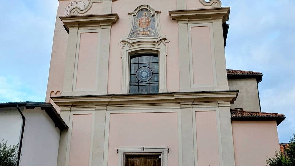 A pink church with a bell tower, a large clock, and a statue of a religious figure.