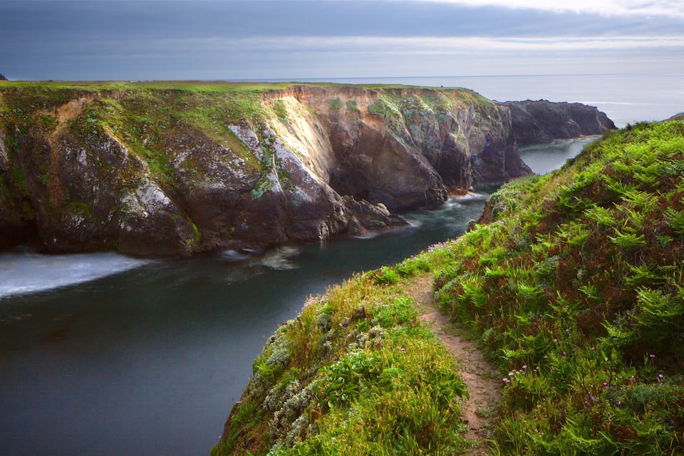 A coastal cliff with a narrow waterway between two steep cliffs.