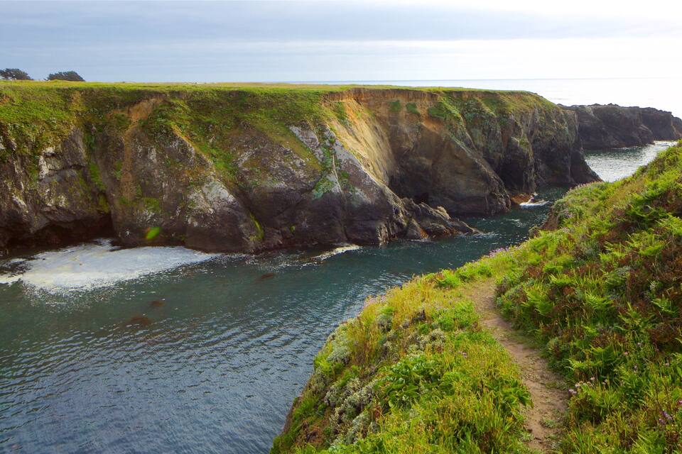 A coastal cliff with a narrow waterway and a grassy path.